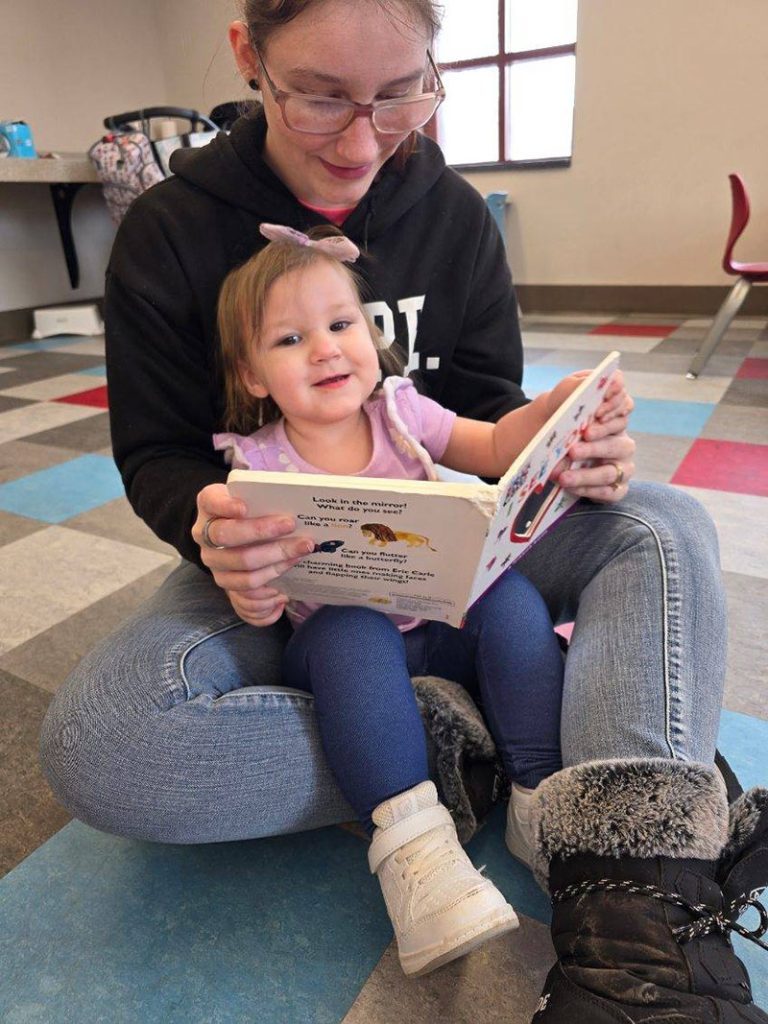 teenage girl reads to infant girl sitting in her lap